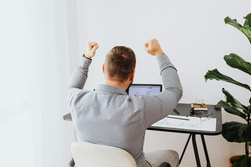 Se préparer à des moments à enjeux - gestion stress et régulation des émotions Un dirigeant confiant et dynamique qui lève les bras en signe de victoire devant son ordinateur : image de la performance mentale atteinte grâce à la sophrologie, visualisation positive et gestion du stress avant une réunion importante, telle que je l'accompagne.