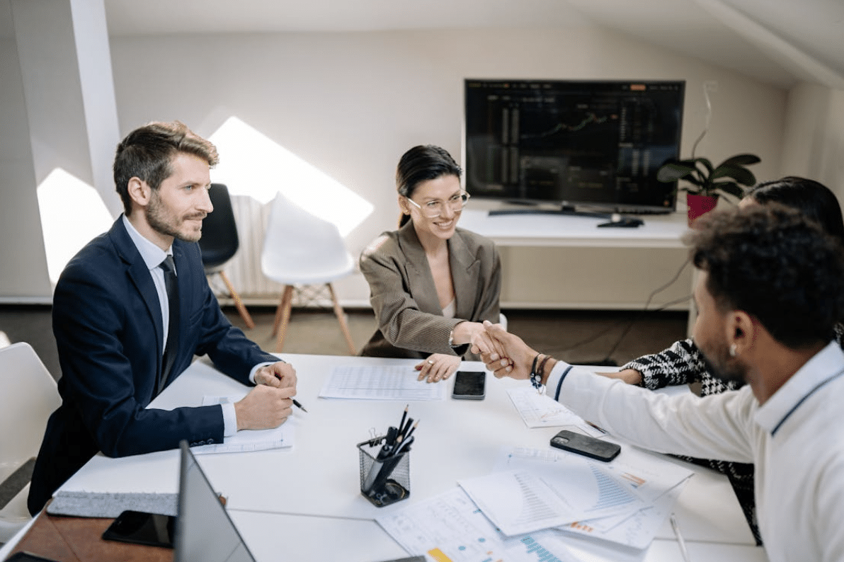 Tout savoir sur le coaching professionnel - réunion tripartite Réunion professionnelle autour d’une table avec poignée de main dans un bureau moderne.