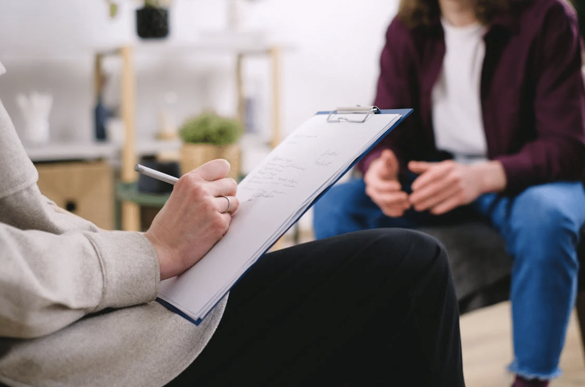 Séance d’accompagnement ou de coaching avec un professionnel Séance d’accompagnement ou de coaching avec un professionnel prenant des notes sur un clipboard face à un client assis.