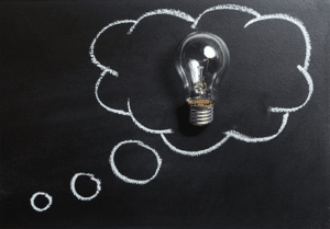 La visualisation mentale en entreprise : un outil de coaching Ampoule dessinée à l’intérieur d’une bulle de pensée tracée à la craie sur un tableau noir, illustrant une idée, une visualisation mentale ou une réflexion.