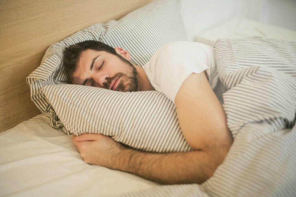 Sommeil réparateur grâce à la sophrologie Homme endormi profondément dans un lit confortable, oreiller moelleux et draps clairs, illustration d'un sommeil réparateur favorisé par la sophrologie : respiration calme et relaxation corporelle pour vaincre les insomnies et réveils nocturnes.